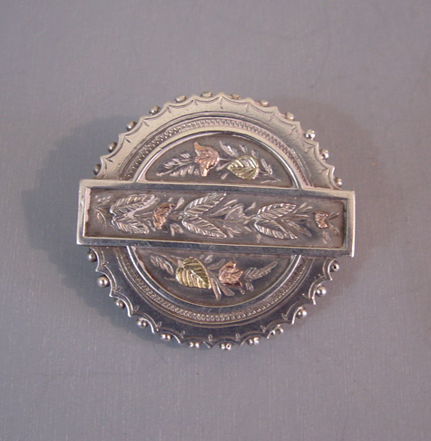 VICTORIAN sterling silver round locket brooch with a rose and yellow gold overlay, a tulips and leaves motif with scalloped edge and fittings for a photo