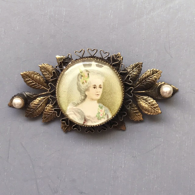 HOBE painted portrait pin set in textured gold tone metal leaves with a glass pearl on each end
