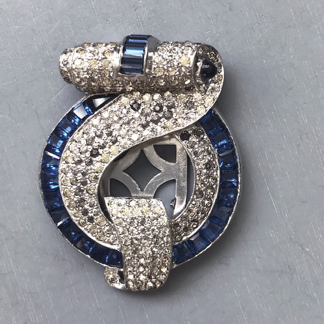 DEROSA dress clip in a lover’s knot design with blue invisibly set baguettes, a blue cabochon at one end and and pave clear rhinestones