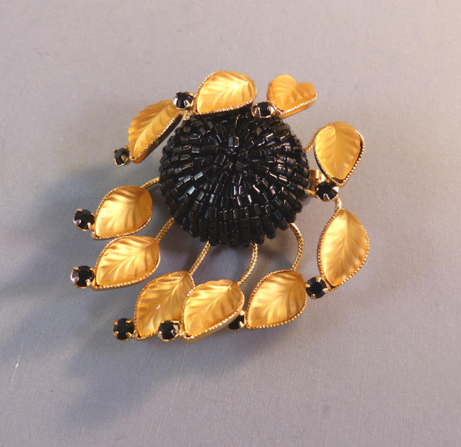 HATTIE CARNEGIE brooch with luminescent pressed golden glass leaves that surround a center of  black glass bugle beads