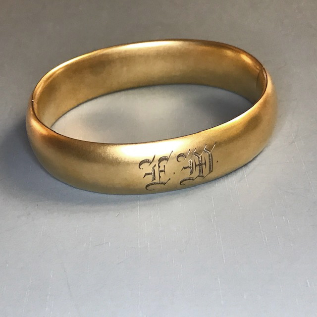 MATTE finish gold colored metal hinged bangle bracelet, engraved with the initials “EM” on the front and “USA 1914” on the inside
