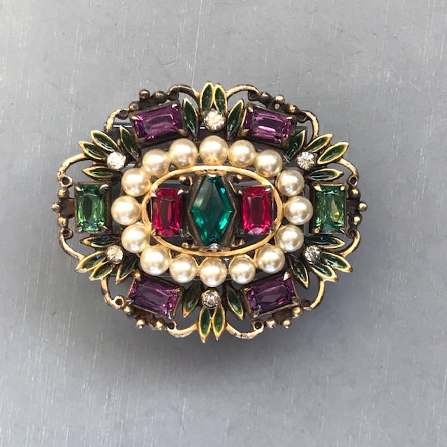 DEROSA brooch with purple, teal, red and pale blue rhinestones and glass pearls and accented with clear rhinestones and tiny green enameled leaves around the edge