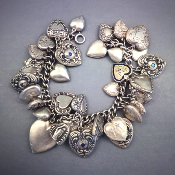 STERLING charm bracelet with 34 puffy heart charms, total length 7". Among others, the charms include: an engraved and enameled forget-me-not