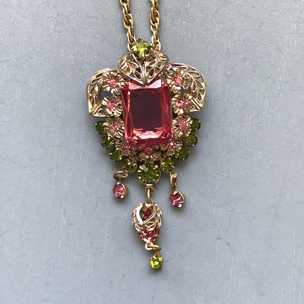 PENDANT of a pink emerald cut rhinestone center with green and pink smaller rhinestones set in a gold tone filigree with dangling rhinestones beneath it