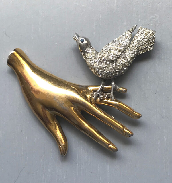 BIRD IN HAND! an unusual gold tone metal hand brooch with a clear rhinestone pave silver bird perched upon the little finger